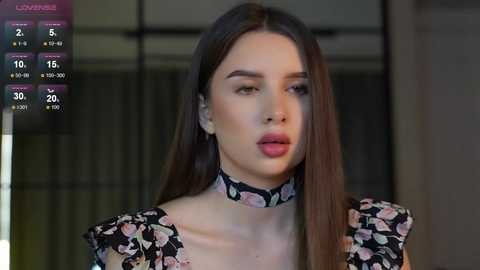 Media: Video of a young woman with long brown hair, wearing a black floral blouse and floral choker, in a dimly lit room.