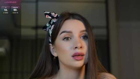 Media: Video of a young woman with long brown hair, wearing a floral headband and pink lipstick, looking serious.