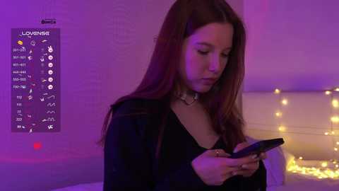 A video of a young woman with long brown hair, wearing a black top and a choker, focused on her smartphone in a dimly lit room with purple and yellow lighting.