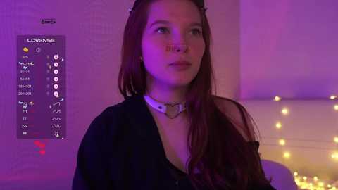 Video of a young woman with long red hair, wearing a black shirt and silver choker, against a purple-lit background with a digital menu overlay on the left.