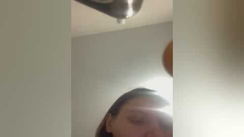 Video of a woman with long brown hair, partially obscured by a mirror, in a dimly lit room with a bright, circular light fixture overhead.