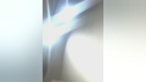 Media: Video of a blurred, abstract figure, possibly a person, with a bright light source creating a lens flare effect in the background. The image has a soft, out-of-focus quality, emphasizing light and shadow rather than specific details.