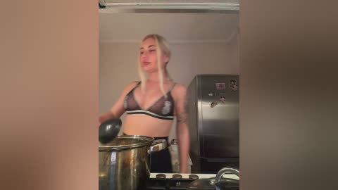 A video shows a blonde woman in a black lace bra, stirring a pot on a stove in a dimly lit kitchen.