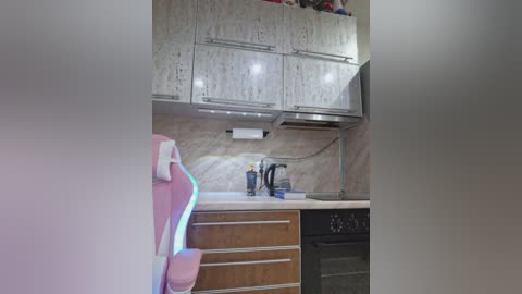 Media: Video of a modern kitchen with white cabinets, a pink gaming chair, and a stove.