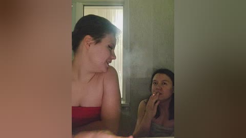 Media: Video of two women in a dimly lit room; one with fair skin and red dress, the other with darker skin and grey top, smoking a cigarette, both in profile.