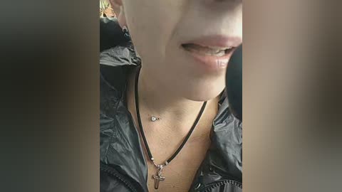Video of a close-up, cropped headshot of a young woman with fair skin, wearing a black jacket and necklace, smiling with braces.