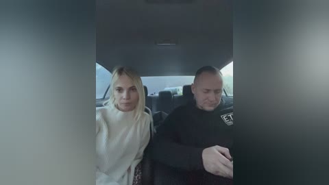 Media: Video of a blonde woman in a white sweater and a bald man in a black shirt sitting in a dimly lit car.