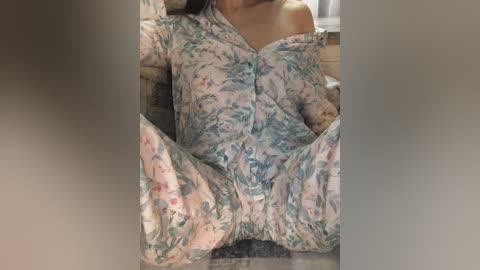 Media: Video of a person in a floral-patterned, off-shoulder nightgown, sitting with legs spread, revealing their genitals. Background features a tiled floor and indistinct objects.