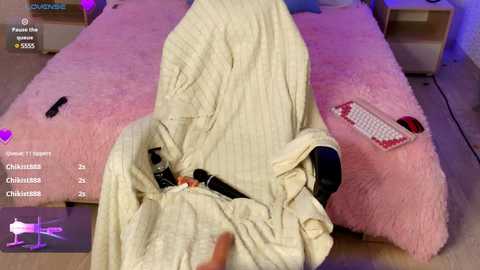 Video of a woman in bed, under a pink blanket, with a video game controller and a small black vibrator visible.