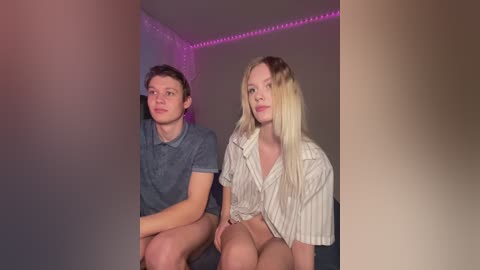 Media: Video of a young Caucasian couple with fair skin, sitting close together. He's in a grey polo, she's in a striped shirt, both looking into the camera.