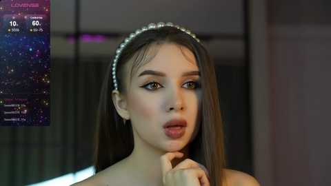 Media: Video of a young woman with long brown hair and a pearl headband, wearing dramatic makeup, looking surprised. Background shows a digital screen with \"Love Island\" text and a countdown.