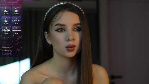 Media: Video of a fair-skinned woman with long, straight brown hair, wearing a silver headband, and a strapless dress, indoors, with a virtual weather overlay.