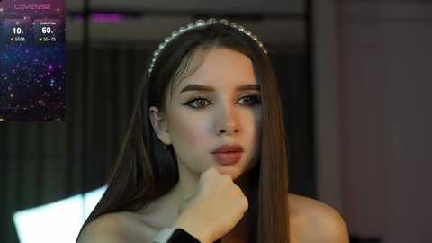 Media: Video of a young woman with long brown hair, wearing a silver headband, and black dress, looking thoughtful, in a dimly-lit room.