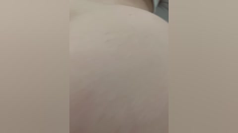 A close-up video of a person's bare, pale buttocks and upper thigh, showing skin texture and a slight red mark. The background is blurred and neutral-colored.