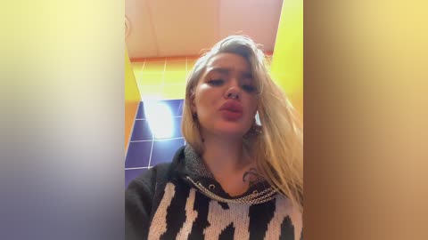 Video of a blonde woman with pouty lips and heavy makeup, wearing a zebra-print sweater, in a brightly lit, colorful bathroom with tiled walls.