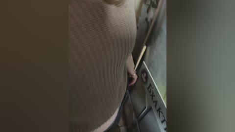 Media: A dimly-lit video shows a close-up of a woman's bare breast, partially obscured by a beige, textured sweater. The background is blurred, suggesting an indoor setting.