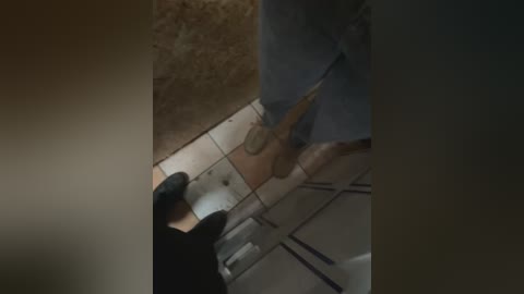 Media: A video captures a person wearing blue jeans and black gloves taping a wooden plank to a white-tiled floor. The setting is indoors with a grassy area visible in the background.