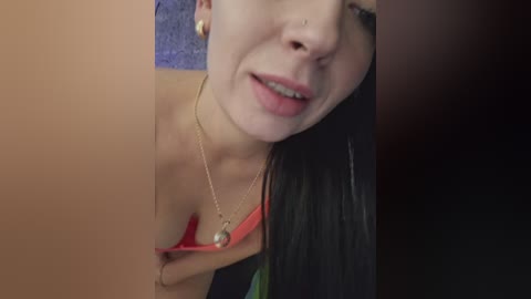 Video of a young woman with light skin and long black hair, wearing a red strapless top, revealing her breasts, and a gold necklace, against a purple carpet background.