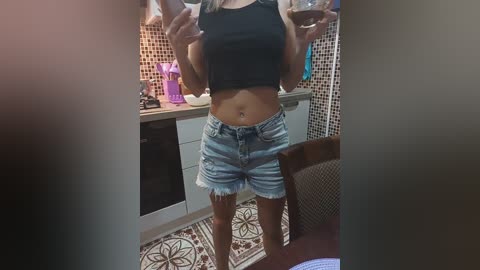 Media: Video of a woman in a kitchen holding wine glasses, wearing a black crop top and frayed denim shorts. Background includes a tiled floor, counter, and purple drink bottles.