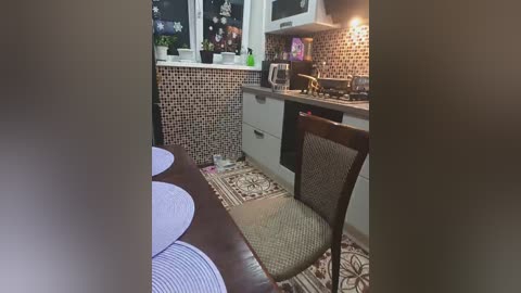 Media: Video of a cozy, small kitchen with beige tiles, dark wooden chair, white cabinets, and a brown table with blue placemats, lit by warm lighting.