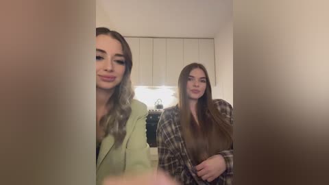 Media: A video of two young women in a modern kitchen. One wears a green jacket, the other a plaid shirt. They stand in front of white cabinets and a countertop with a kettle.