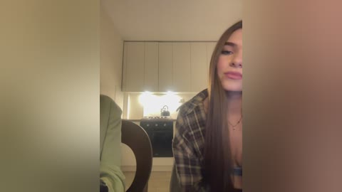 Media: A video of a young woman with long brown hair, wearing a plaid shirt, standing in a dimly lit room with a vanity mirror, light bulbs, and a dresser in the background.