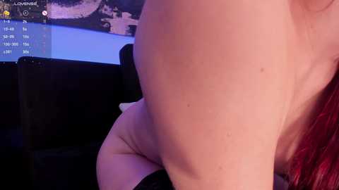 Video of a naked person with fair skin, bent over a couch. The background features a dark couch and a TV showing a live stream with the \"LOVING\" text.