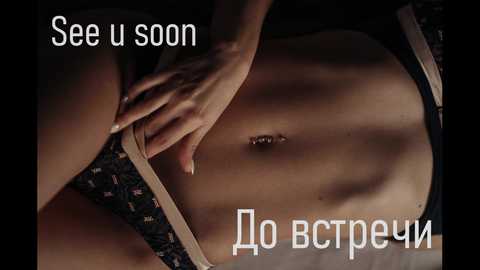 Media: Video of a woman's bare torso, showcasing a slender physique with light skin. She is lying on a black patterned surface, wearing a beige thong. Her left hand is resting on her stomach. Text in Russian is overlaid.