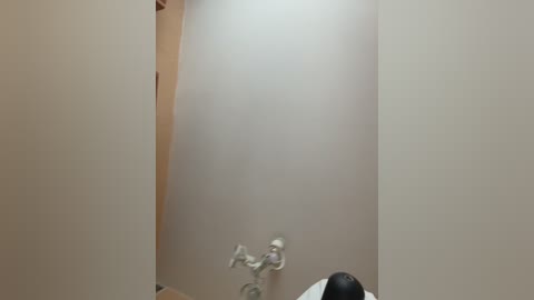 Media: Video of a narrow, beige-tiled bathroom with a single white faucet and a black and white striped towel hanging from a towel rack. The walls and ceiling are plain, contributing to a minimalist, utilitarian feel.