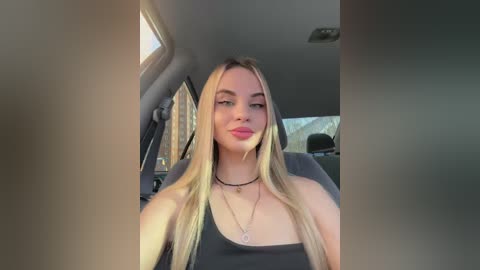 Media: Video of a young, fair-skinned, blonde woman with long hair, wearing a black tank top and multiple necklaces, sitting in a car.