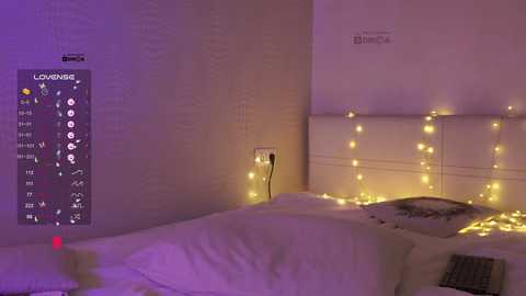 Video of a cozy bedroom with a white bed adorned with a decorative pillow, soft yellow string lights, and a colorful digital clock displaying a calendar.