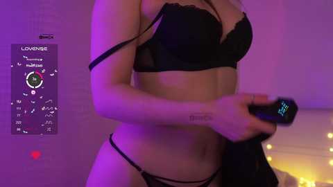 Video of a light-skinned woman with small breasts wearing black lace lingerie, holding a vibrator in a dimly lit bedroom.