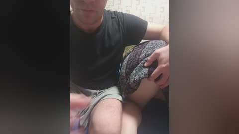 A video shows a man in a dark T-shirt and shorts, lifting a woman's skirt, revealing her bare buttocks, in a dimly lit room with wallpaper.