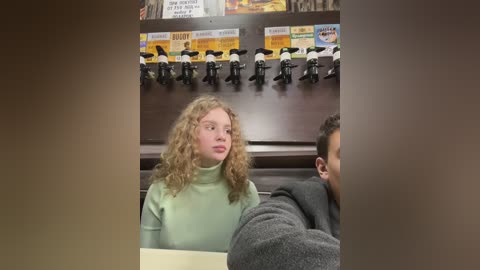 Media: A video of a young woman with curly blonde hair, wearing a green turtleneck, sitting next to a man in a gray sweater, in a fast-food restaurant with toy police officers on the wall.