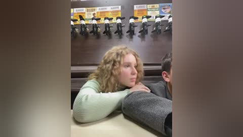 Media: Video of a young, curly-haired girl in a green sweater, leaning on a man's leg in a dark room with a wall-mounted sign and numerous black-and-white motorcycle figurines.