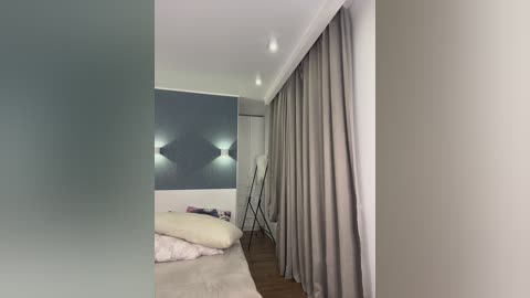 Media: Video of a minimalist bedroom with a large, abstract painting on a gray wall, a bed with light-colored bedding, and floor-to-ceiling gray curtains.