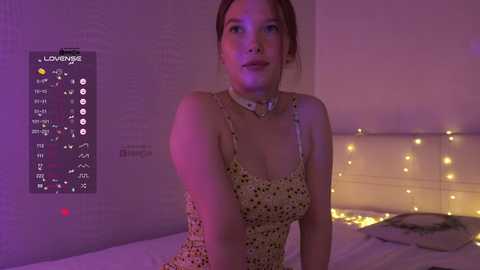 Video of a young woman with light skin and brown hair, wearing a floral dress, in a dimly lit bedroom with purple lighting, \"Love\" wall art, and string lights.