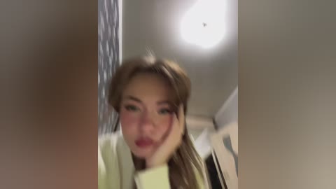 Media: A blurry video of a young woman with light skin and brown hair, wearing a light-colored top, standing in a bathroom with a shower curtain.