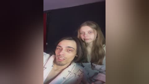 Media: Video of a young man with long hair, wearing a white robe with stars, and a young girl with long brown hair, both with serious expressions.