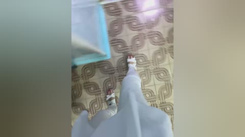 Media: A video shows a white person wearing white socks and black shoes walking on a patterned beige carpet. The background features a blue object and a white wall.