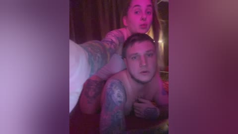 A video showing a tattooed man with a pale complexion, topless, and a woman with light skin and long brown hair in a dimly lit room.