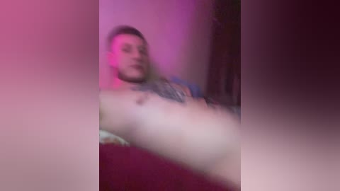 A blurry video of a nude man with a muscular physique and a tattoo on his chest, lying on a bed, bathed in pink and purple lighting.