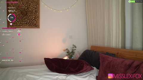 A video of a cozy bedroom with a wooden headboard, white walls, a maroon throw pillow, and fairy lights.