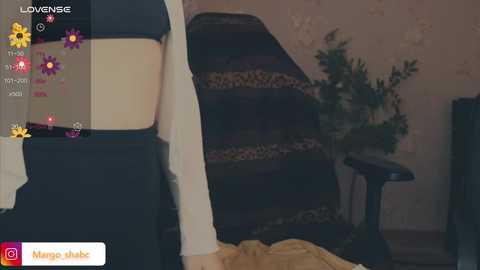 A video of a woman in a black top and shorts, standing in a dimly lit room with a patterned armchair, a potted plant, and a TV.