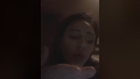 A dimly-lit video shows a young woman with long dark hair, pale skin, and red lipstick, leaning forward with her eyes closed, creating a moody, intimate atmosphere.