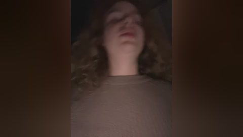 Media: Video of a woman with shoulder-length, curly brown hair lying on her back, wearing a beige shirt. The image is blurry, making it difficult to discern details clearly.