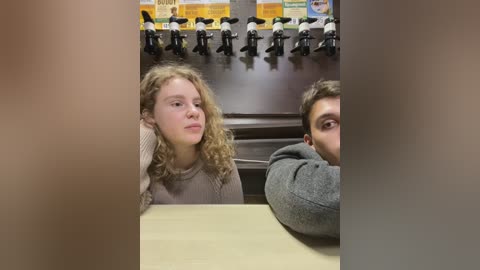 Media: Video of two young people in a dimly lit restaurant, with a blonde girl in a beige sweater and a boy in a gray hoodie, both looking tired.
