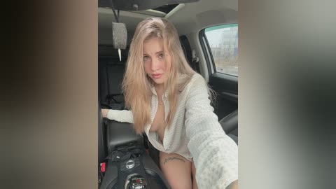 Video of a blonde woman in a white sweater, partially unbuttoned, sitting in a car with a distressed expression.