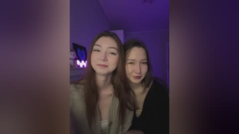 Media: Video of two young women with fair skin and brown hair, smiling, wearing casual attire in a dimly lit room with purple lighting.