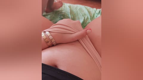 Video of a person with fair skin, wearing a pink ribbed dress, and a gold watch, lying on a green sheet. The image is cropped and blurred, focusing on the thighs and lower abdomen.